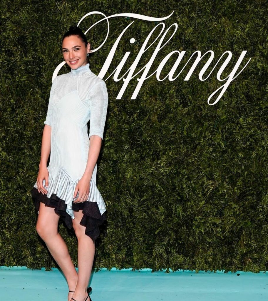 Gal Gadot wearing a white dress and posing in front of Tiffany.