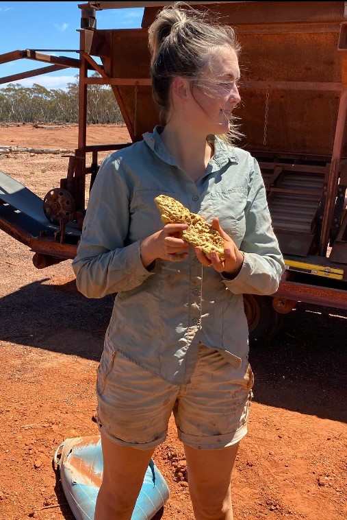 Tyler Mahoney holding gold in her hand and looking at another side.