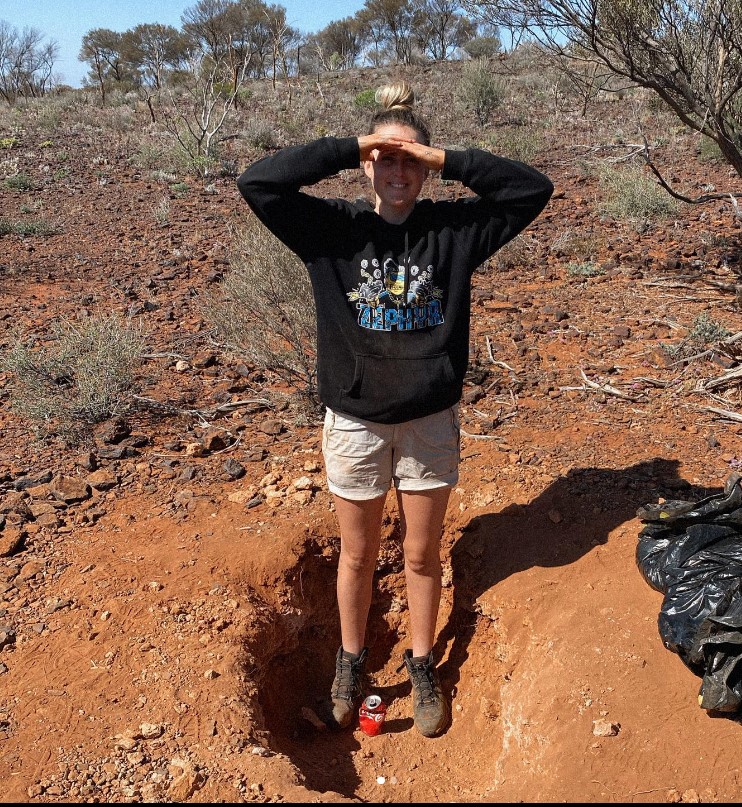 Tyler Mahoney standing at one of the gold fields. She is wearing a black sweatshirt and brown shorts.