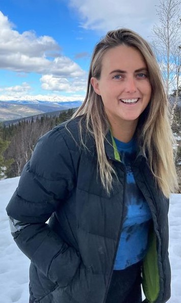 Tyler wearing a blue shirt an black jacket. She is standing in a land covered with snow.