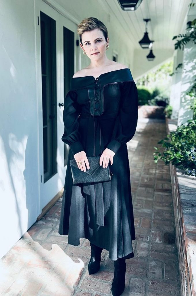 Ginnifer Goodwin wearing black dress and black boots, holding a black handbag.