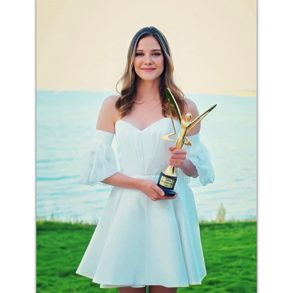 Alina wearing a white dress and holding an award