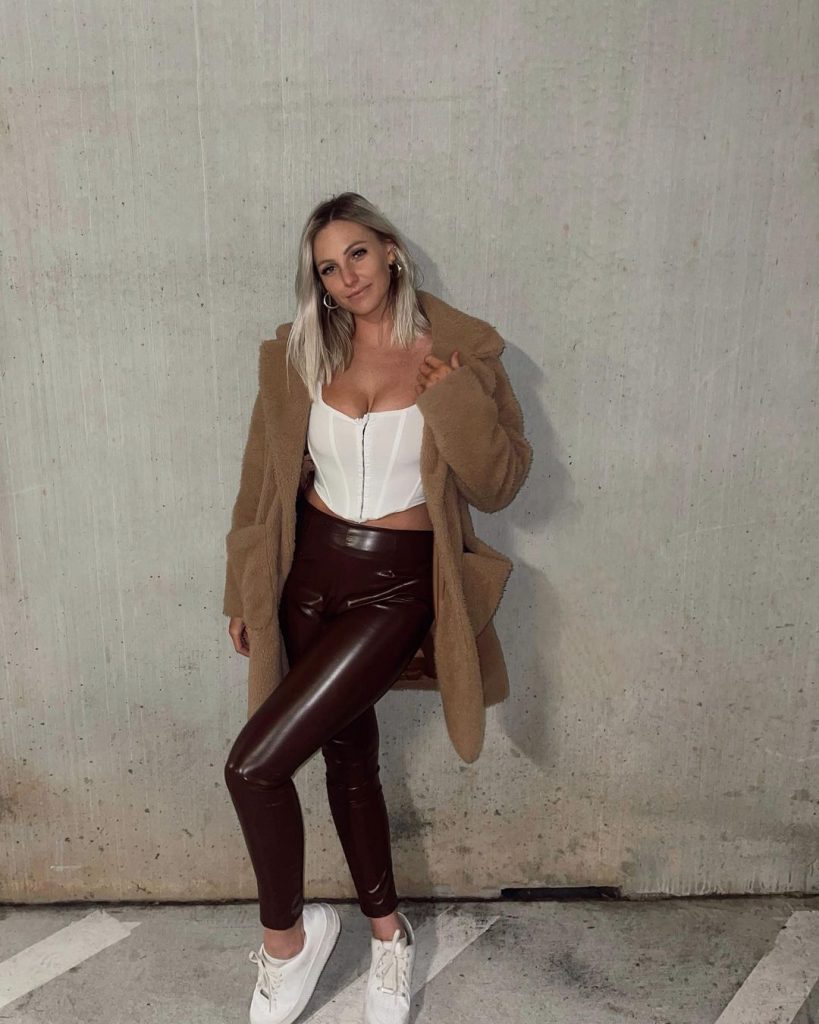 Harper wearing a black jegging with white bardot top with brown coat.