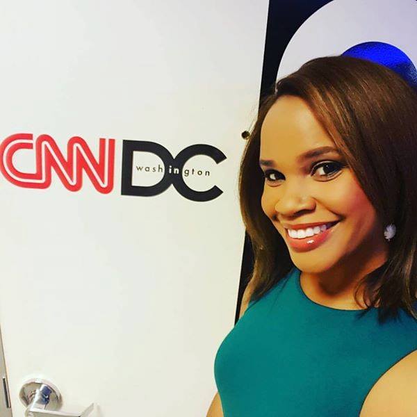 Laura wearing green dress and taking selfie in front of logo of CNN DC logo.