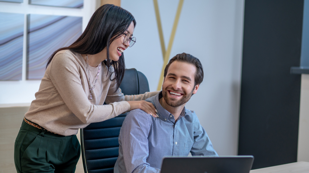 A girl talking to a boy in office touching his shoulders.