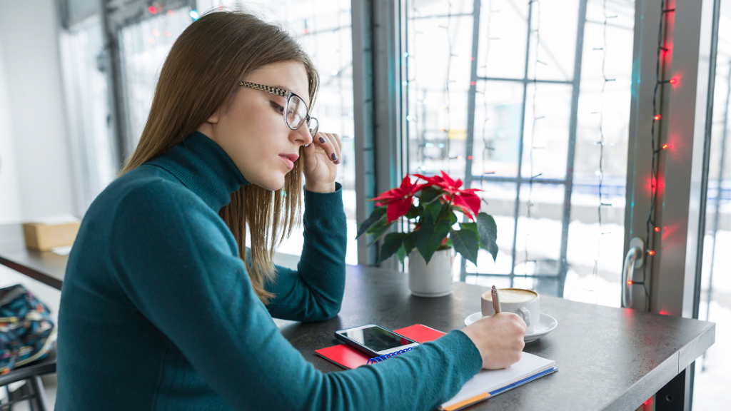 A girl wearing glasses writing something on her notebook.