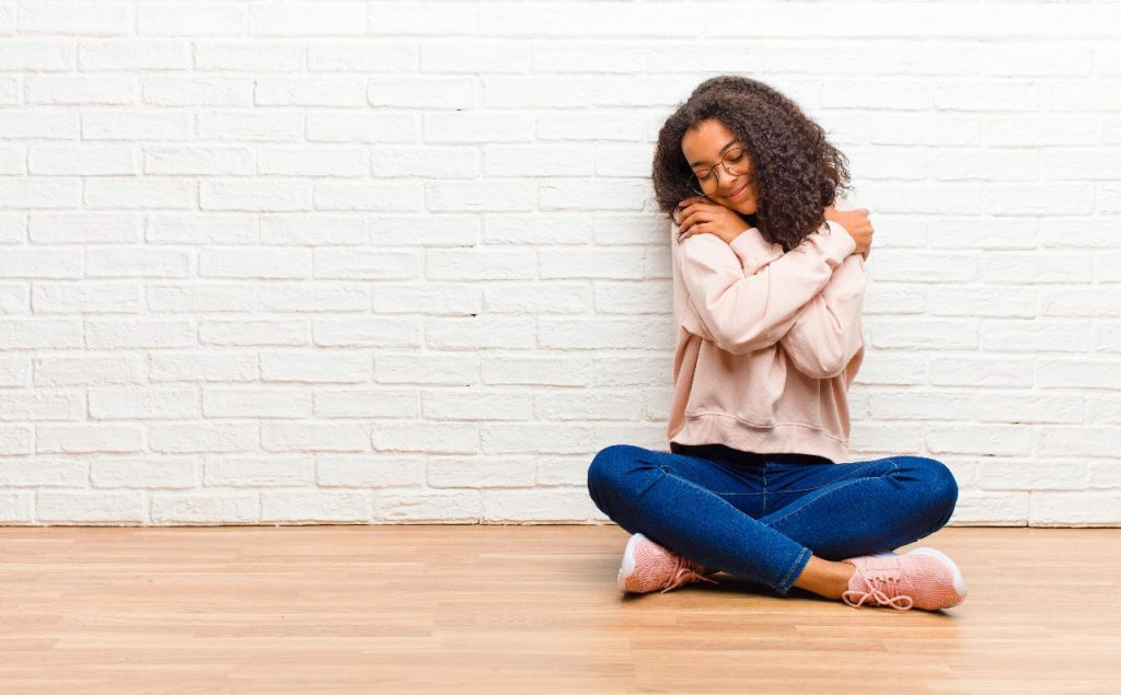 A girl folded her hands around her shoulders while sitting on the floor.