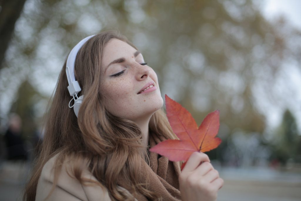 A girl holding a leaf and wearing headphones.