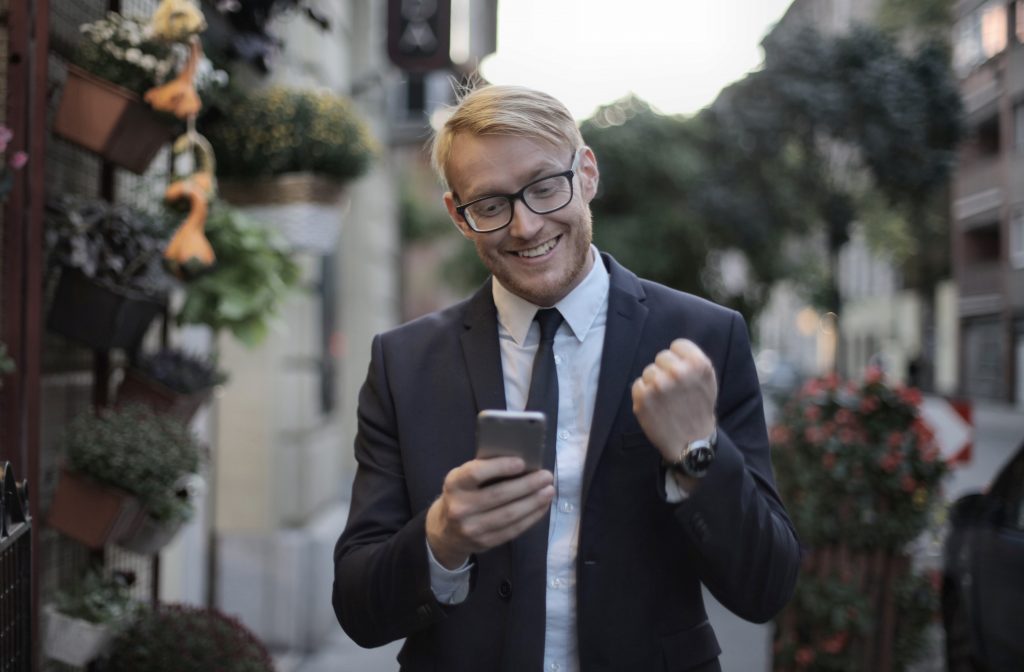 A man wearing white shirt and black happy and smiling while looking in his phone.