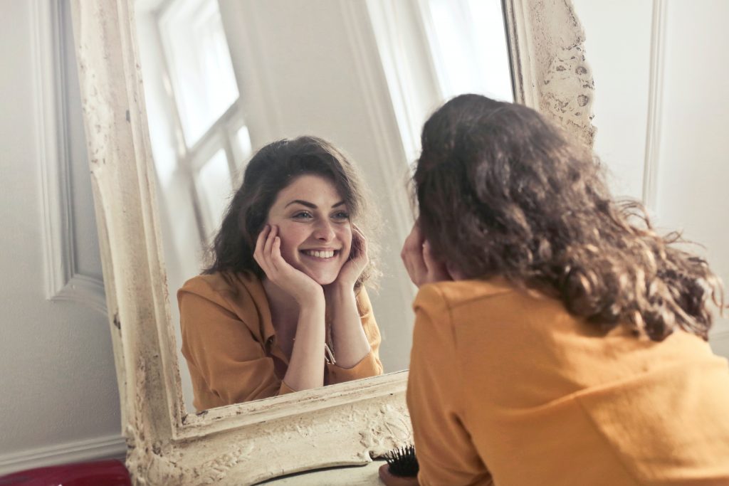 a girl looking at herself in mirror.