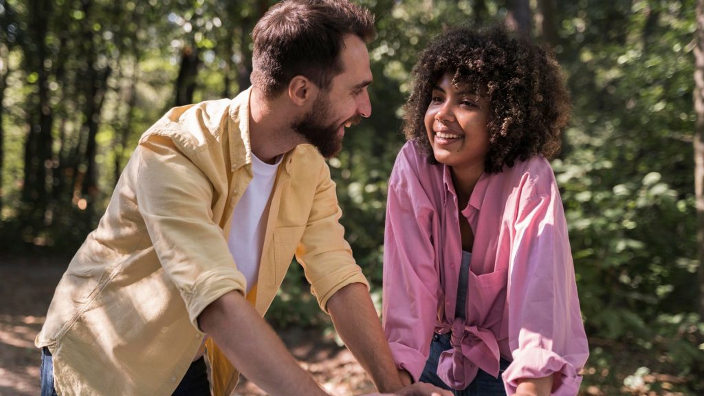 couple smiling at each other while taling in the middle of woods.