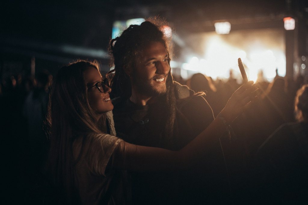 Young happy couple having fun and taking selfie with a smartphone at music festival. Young and cheerful couple on a music festival.