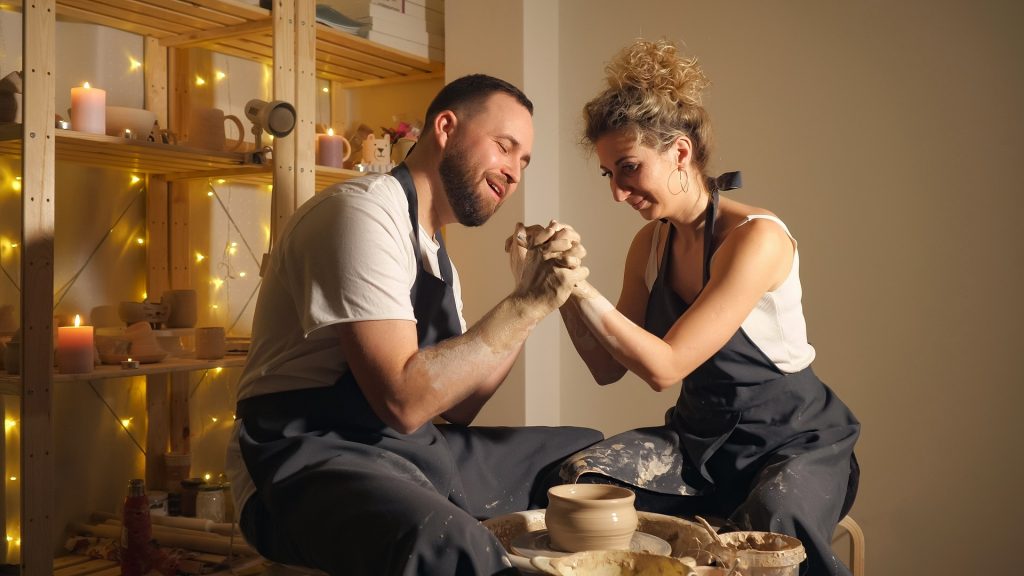man and a woman making clay jug on potter's wheel.