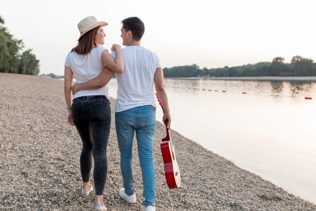young-couple-carrying-guitar-walking-away-beach 
