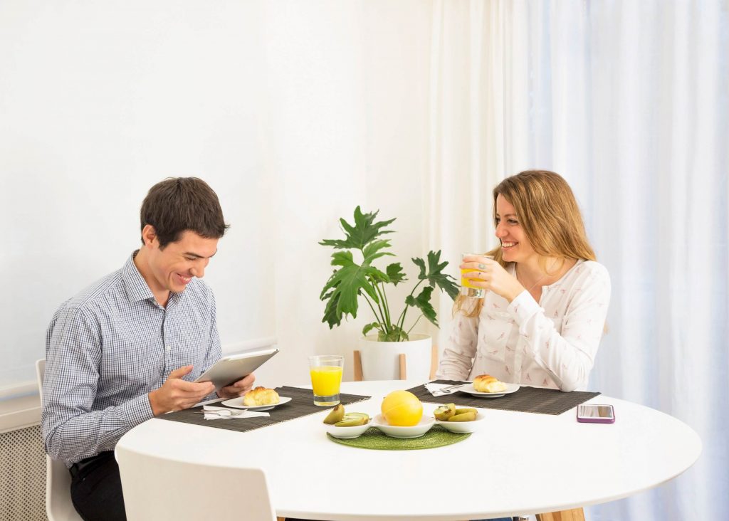 young-woman-looking-smiling-man-using-digital-tablet-breakfast-table